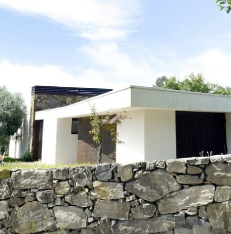 Volume branco com portada escura sobre muro de granito